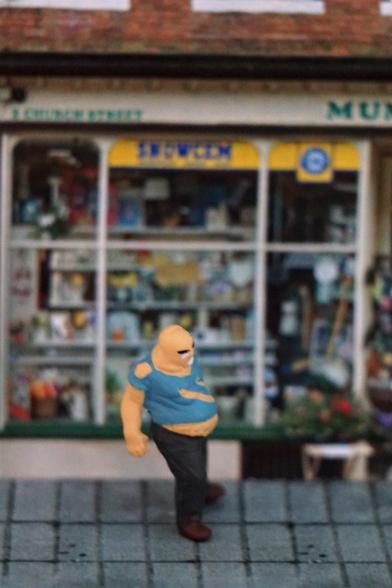 A tiny 00 scale zombie figure standing outside a photo of a local shop