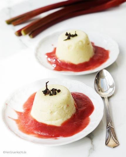 Zwei Vanille-Puddinge auf weißen Untertassen. Um die Puddinge Rhabarbermousse.
