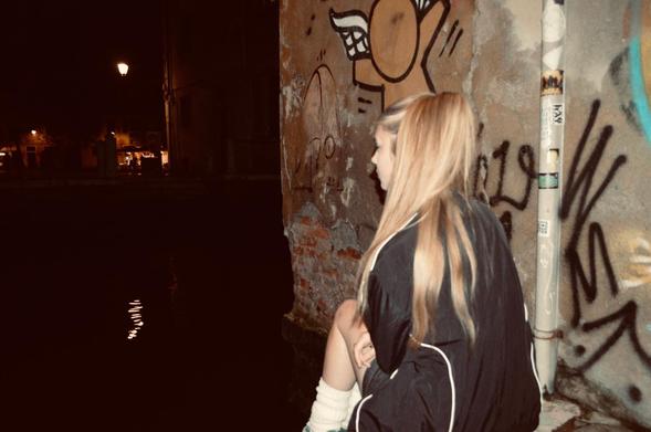 A girl with long blonde hair sits with her back to the lens, looking into the distance.