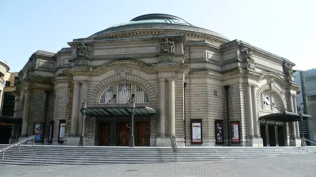 The image shows a grand historical building with an ornate facade, featuring large arched windows and detailed architectural elements. The structure appears to have a prominent entrance with stairs leading up to it, and there are posters displayed on the exterior walls. This type of building is typically associated with theaters, concert halls, or similar cultural venues. The surrounding area looks well-paved and modern, suggesting a vibrant urban setting.

Image Credits: Wikimedia / Kim Traynor / CC BY-SA 3.0