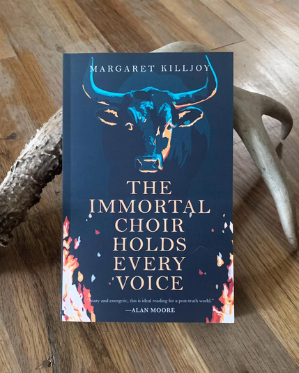 A photo of Margaret Killjoy's novella "The Immortal Choir Holds Every Voice", propped up on a deer antler. The cover features an illustration of a bull flanked by flames over an endorsement from writer Alan Moore that reads "Scary and energetic, this is ideal reading for a post-truth world."
