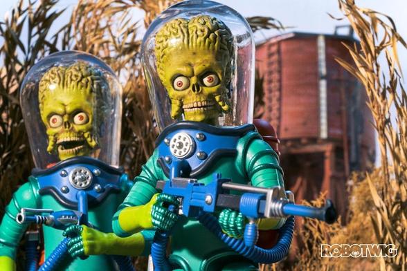 Two Martians holding weapons walk through a cornfield, water tower in distance.