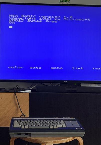 A MSX Canon V-20 from  the 80s connected to a modern TV. On the screen it displays a blue screen with the text: MSX BASIC version 1.0. Copyright 1983 by Microsoft 29915 Bytes free.