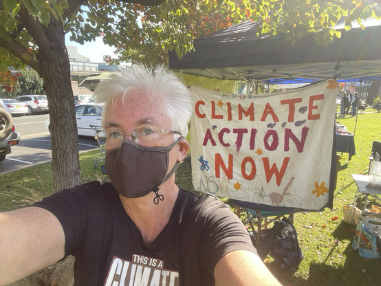 Masked woman in front of a homemade Climate Action Now sign