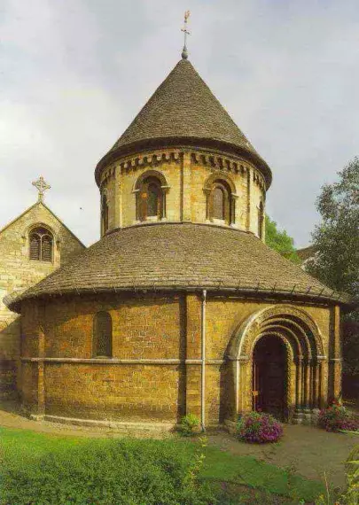 The image features a round building, likely a church or chapel, characterized by a conical roof and arched doorways. The stone construction suggests it may have historical significance, possibly from the Romanesque or medieval period. Surrounding vegetation and flowers add to the picturesque setting. The architectural details indicate careful design, typical of religious structures.

Image Credits: Wikimedia / Noles1984 / CC BY-SA 3.0