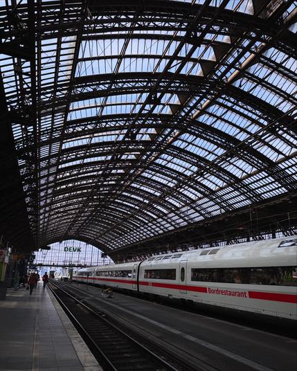 A train station with an arched glass roof, featuring a sleek train along the platform