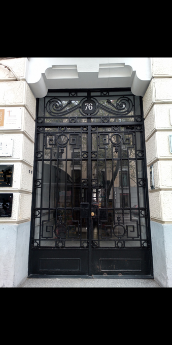 A black decorative metal door with glass panels and the number 76