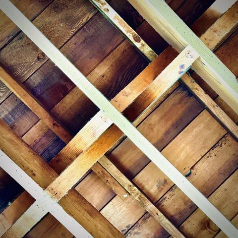 A wooden ceiling's framework/bracing forms multiple diagonal, symmetrical "X" patterns above.