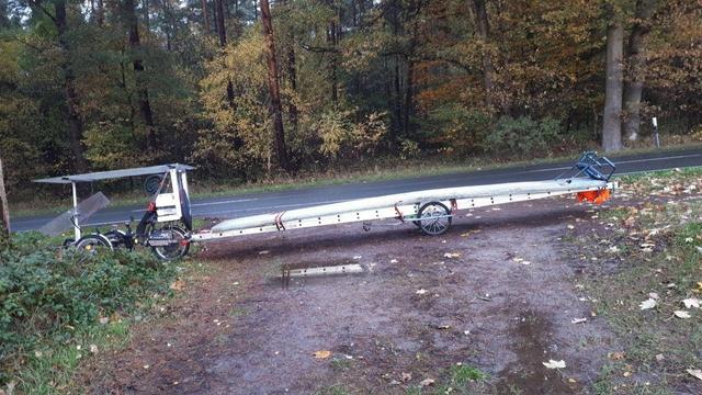 Ein Lastenrad mit einem Fahrradanhänger, auf dem eine Leiter befestigt ist, steht an einer Straße.