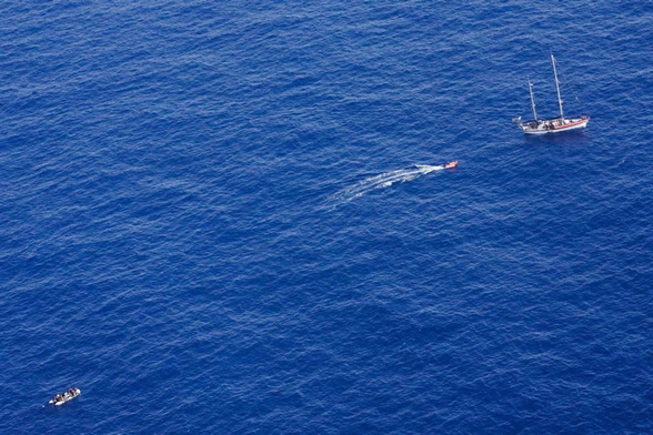 Aufnahme aus der Luft. Links unten das treibende Schlauchboot voller Menschen. Rechtsoben liegt die NADIR. Dazwischen das Beiboot, das gerade zum Segelschiff zurückkehrt.