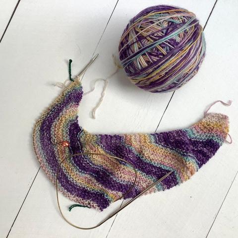 The start of an asymmetrical shawl in garter stitch, it has stripes in various pastel colors.