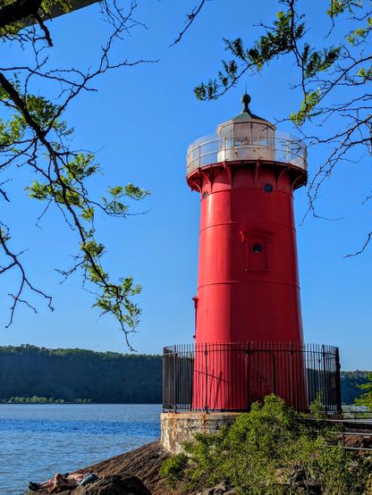 A small red lighthouse on the bank of the river.