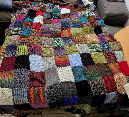 A very colorful knitted patchwork blanket consisting of many 10 by 10 cm squares. The squares are in all sorts of colors and textures, but there is definitely a mossy green overtone.