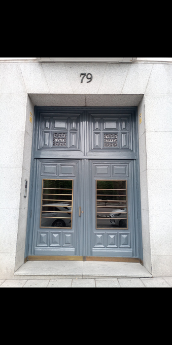 A wooden set if doors painted grey with a large glass panel with metal supports. In the glass are reflections of cars and above is the number 79
