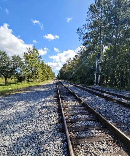 Pair of rusty old train tracks on a bed of grey gravel beneath big blue Florida sky with fluffy white clouds.