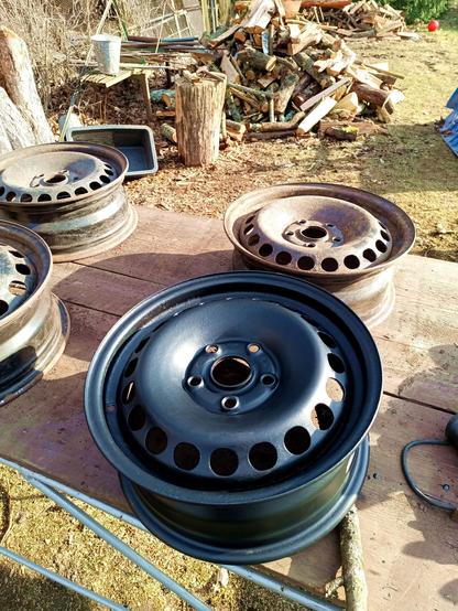 Four wheels on a table outside. Three still rusty, one cleaned up and painted with rust converting primer.