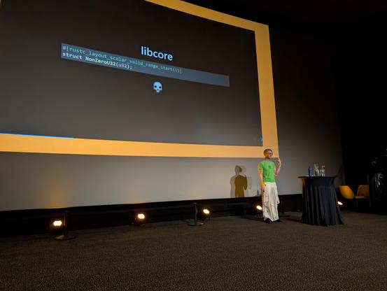 A big screen with a black slide showing the code of struct NonZero and Oli-Obk on the bottom right
