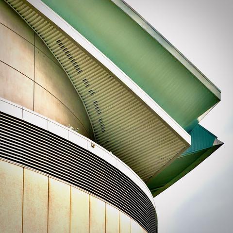 A top exterior corner of the Moda Center stadium angles outward and glows emerald green on its underside beneath a cloudy sky.