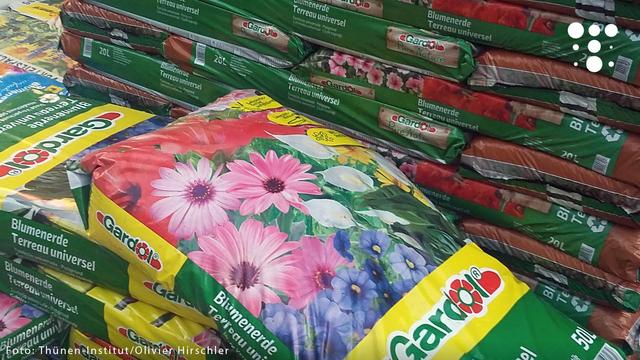 Das Bild zeigt gestapelte Säcke mit Blumenerde in einem Baumarkt oder Gartencenter. Die Verpackungen sind bunt gestaltet, teilweise mit Blumenmotiven (rosa, weiße und blaue Blüten) und in verschiedenen Größen (z. B. 20 L und 50 L) erhältlich. Im Vordergrund liegt ein Sack mit der Aufschrift „Blumenerde Terreau universel“.

Oben rechts ist das Logo des Thünen-Instituts zu sehen.
Am unteren Bildrand steht die Quellenangabe:
Foto: Thünen-Institut / Olivier Hirschler.