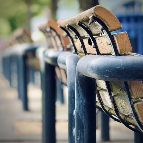 Numerous consecutive groups of two wooden benches with metal, bolted rear supports sit down a line that blurs into the distance on an overcast day.