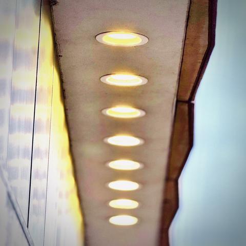 A thin exterior overhang holds eight bright tungsten lights centered in frame from top to bottom under an overcast sky.