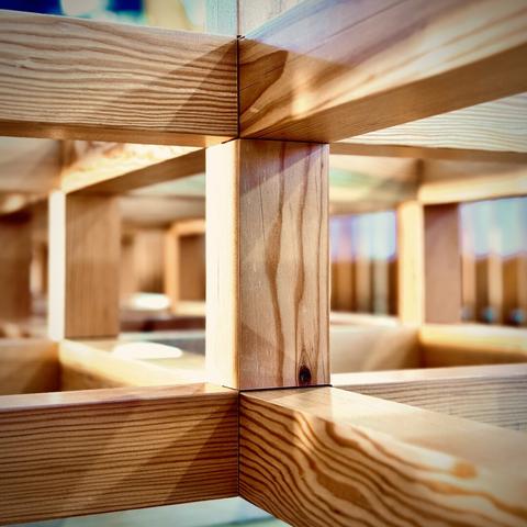 Numerous two-by-two wooden boards intersect from all sides, forming a maze-like framework within an unknown interior space.