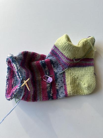 Sock with lime color heel tab and heel en stripey foot in pinks and blues. It's knitted cuff down and approaching the start of the toe.