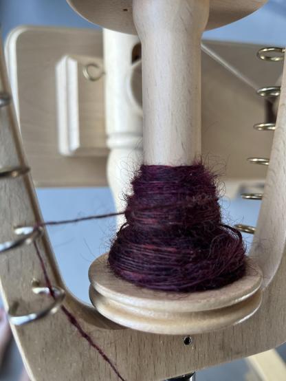 Tiny bit of singles on a wooden bobbin. The yarn has a deep burgundy color that is far more interesting in real life.