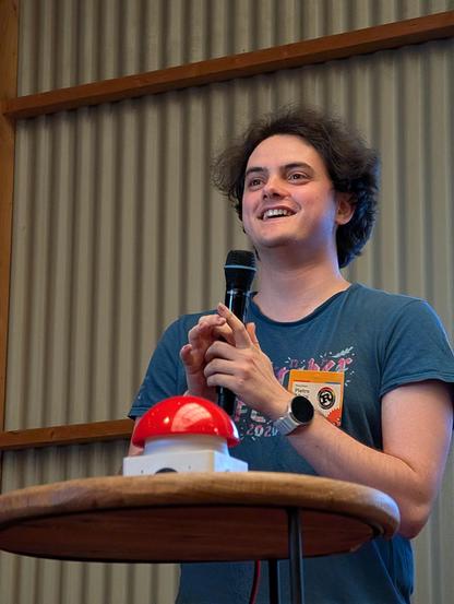 A portrait of Pietro Albini smiling, holding a microphone, begging a big red button