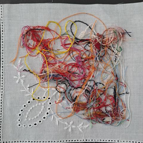 Ein paar Fadenreste aus der textilen "Mülltüte" auf einem Viertel eines Taschentuchs zum Umhäkeln.