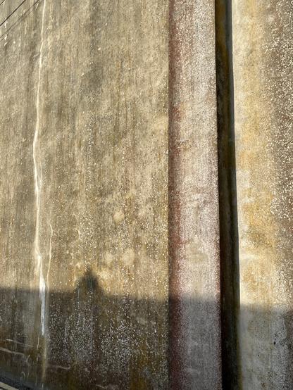 A stippled concrete wall -- light tan -- contains a light red section running vertically through the frame. To the left of the frame a white crack runs the entire frame from top to bottom.