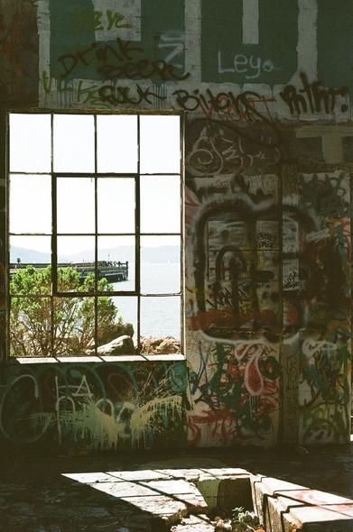 Light streams through an open window casting light in a graffiti tagged abandoned ferry landing warehouse.