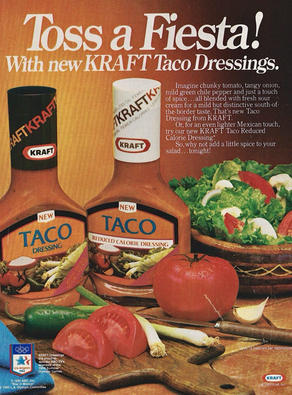 Two bottles of taco dressing. On the far left just says taco dressing. While the bottle next to it says taco reduced calorie dressing. There’s a picture of a salad, tomatoes, and other cut up vegetables.