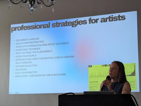 Meryl Pataky in front of a slide of "Professional Strategies for Artists" with strategies listed below projected behind her