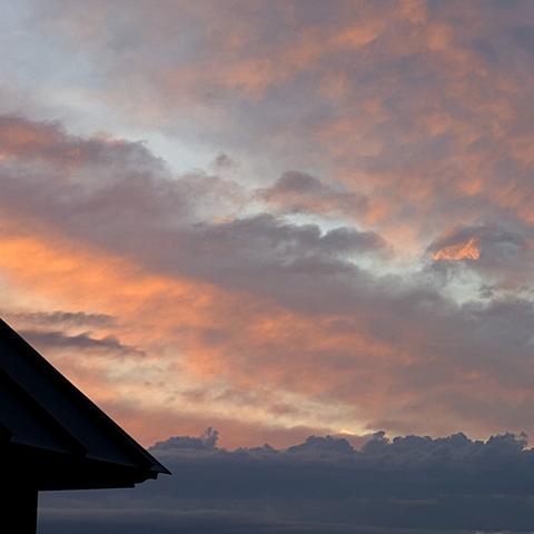 Sunlight glows a pale orange in areas of fluffly gray clouds above. Dark blue-gray clouds lurk lower.