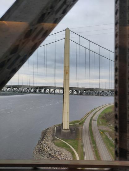 Foto. Eine Hängebrücke, im Vordergrund Stahlfachwerkträger einer weiteren Brücke.