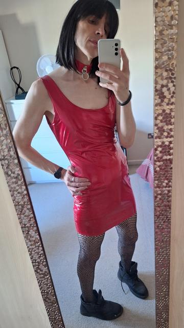 Non binary person in a shiny red dress, collar and fishnet tights