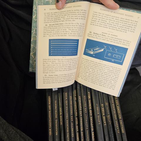 A collection of textbooks from The International Library: International Texybook Company, Scranton PA. 
An open book is "Elements of Blueprint Reading". 
The spjnes of the others visible read left to right: 
Gear Calculations and Making
Measuring Instruments
Milling-Machine Practice and Work
Geometry and Trigonometry
Tempering and Heat Treatment of Steel
Milling Machines and Equipment
Grinding Equipment and Practice
Shapers, Slotters, and Boring Mills
Lathe Work-I
Lathe Work-II
Lathe Work-III
Planers amd Planer Practice
Drilling Machines and Practice