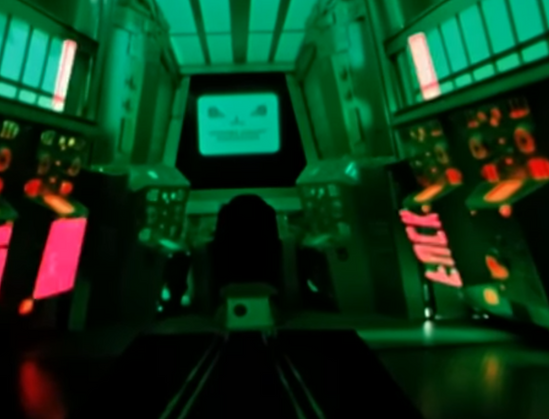 This screenshot is from science fiction film "Dark Star". It shows the interior of the control room bathed in green light. In the center, there's a monitor or screen displaying what appears to be a sinister-looking face or entity with a menacing smile. A silhouette of a person can be seen from behind, sitting in front of this screen. The room has various control panels with colorful lights (primarily red, pink, and orange) on both sides. The overall atmosphere is eerie and tense, creating a sense of technological threat or confrontation. At one point the mirrored letters "FUCK" can be seen as bright red lights. [mostly by claude]