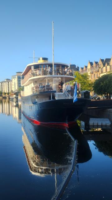 Large yacht converted into a floating hotel and restaurant, casting its reflection into the river on a sunny evening