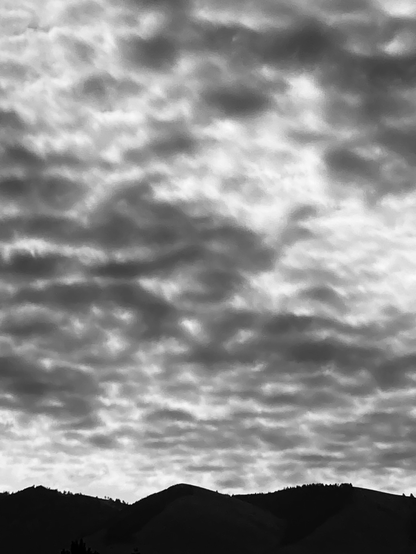 In a case of silhouettes, mountains are silhouetted in this black and white image. The clouds, which are heavy and covering the sky, are also silhouetted because the sun is rising behind them.