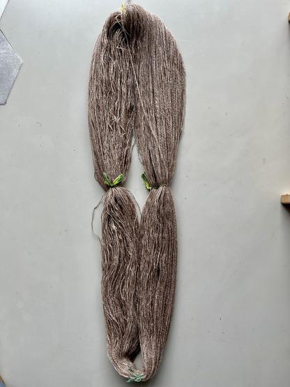 Hank of wet 3-ply yarn in brown and cream shades. It is tied together with four evenly spaced green eight-knots of yarn.