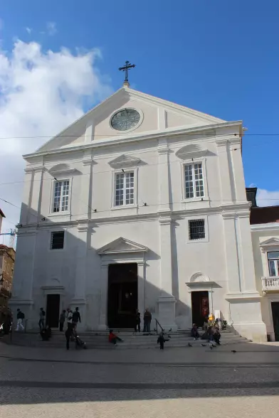 The image depicts a large, white church building with a prominent facade. It features a cross at the top, large windows, and a round window above the entrance. The building appears to be located in a square where people are gathered, and the sky is partly cloudy. The architecture suggests a classical style, typical of many historical churches.

Image Credits: Wikimedia / Uhooep / CC BY-SA 4.0