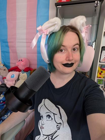Revy wearing black lipstick and purple and white headphones with white pink fluffy cat ears attached and is near a microphone