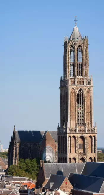 The image features a prominent church tower, likely part of a larger cathedral or church structure, set against a clear blue sky. The architecture appears to be Gothic or Gothic Revival, characterized by intricate detailing and tall, pointed elements. In the foreground, there are rooftops of surrounding buildings, indicating an urban setting. The scene is bright and showcases a mix of historical and modern elements typical of cityscapes.

Image Credits: Wikimedia / Massimo Catarinella / CC BY 3.0