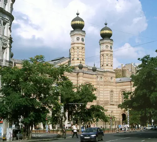 The image features a distinctive architectural structure, characterized by its twin towers with domes. The building appears to be designed in a style that blends elements of both historic and ornate architectural features. Surrounding the building, there are trees and a street, indicating an urban setting. The sky is partly cloudy, adding to the overall atmosphere of the scene. If you have specific questions about the architecture or style, feel free to ask!

Image Credits: Wikimedia / The original uploader was OsvátA at Hungarian Wikipedia. / CC BY-SA 3.0