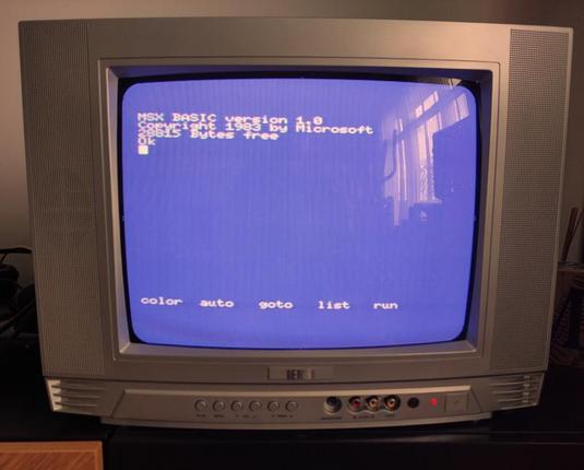 A CRT TV displaying on the screen a blue background with the text: MSX BASIC version 1.0. Copyright 1983 by Microsoft 29915 Bytes free, in white.