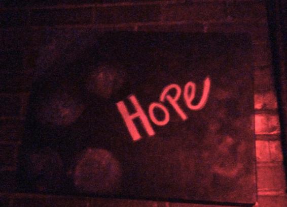 A painting on a brick wall, with the words "HOPE" in pink letters, and some purple spherical shapes.