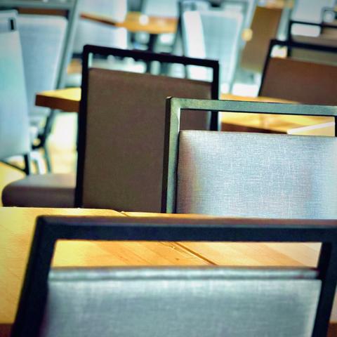 Empty, gray and black metal-framed, linen-backed chairs sit against their respective dining tables, filling the frame with an almost claustrophobic eating experience.