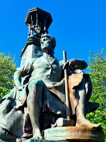 A bronze statue of a seated young man  holding a sledger hammer.